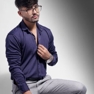Portrait of a fashionable man wearing glasses and a blue shirt against a gray background.